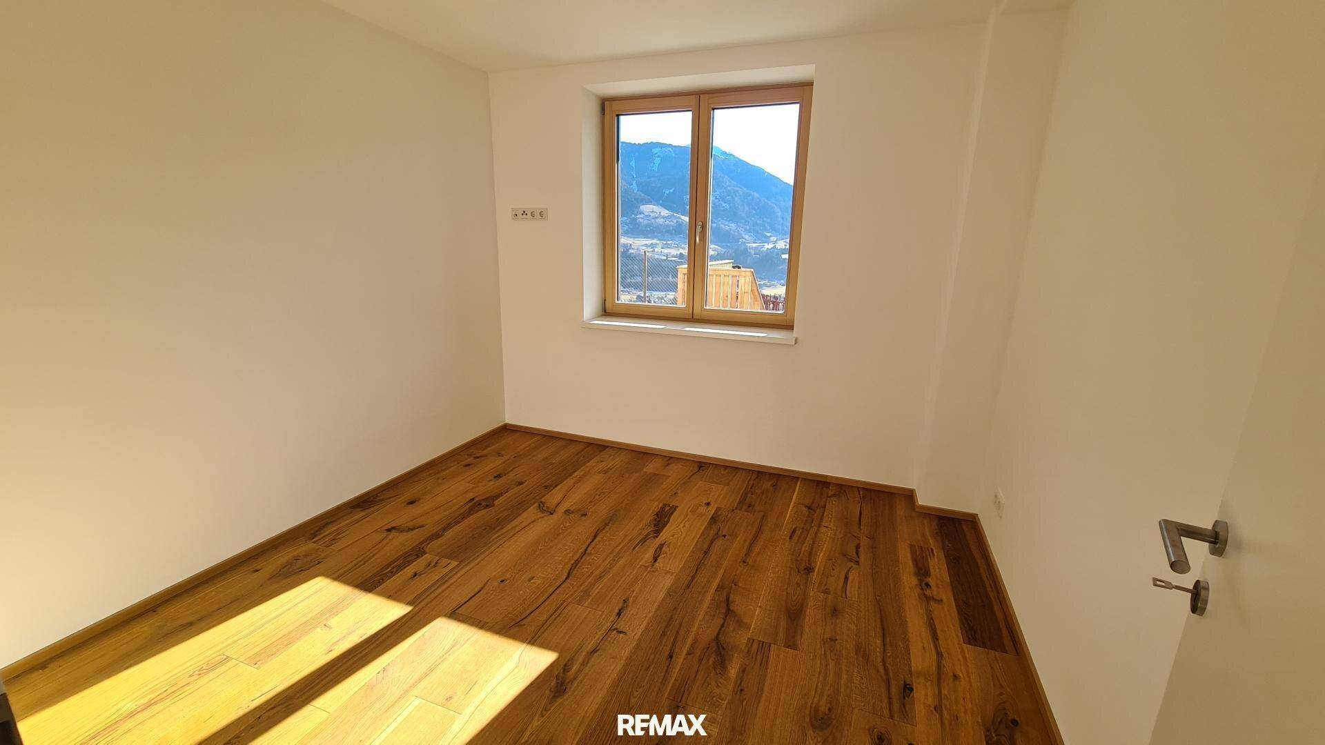 Gemütliches Schlafzimmer mit Holzboden und Fenster, das einen ruhigen Blick auf die umliegende Berglandschaft bietet.