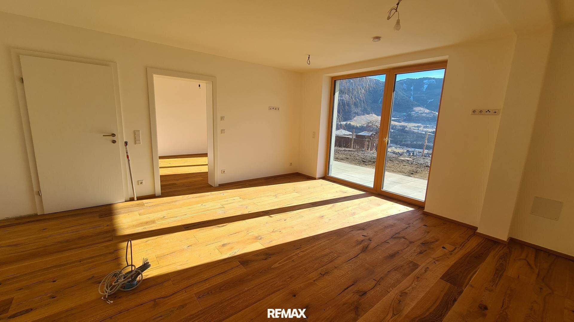 Geräumiger, heller Raum mit Holzboden und großen Fenstern, die einen weiten Blick auf die Berge ermöglichen.