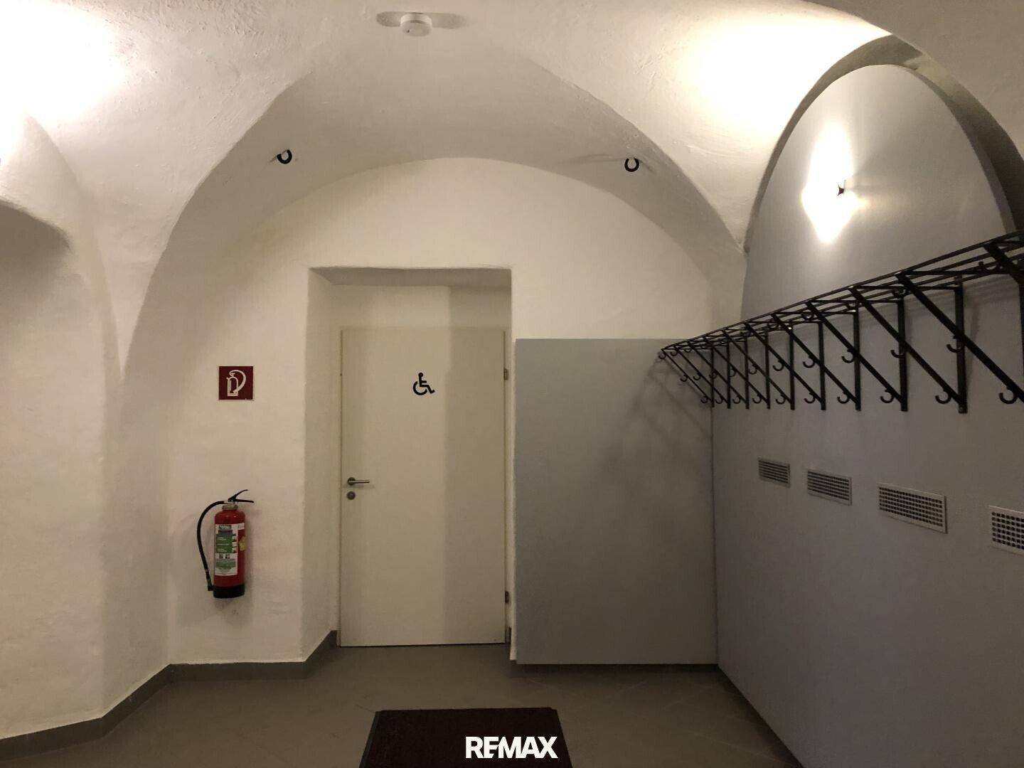 Eingangsbereich mit Gewölbedecke, Garderobe und Hinweisen zur Barrierefreiheit.