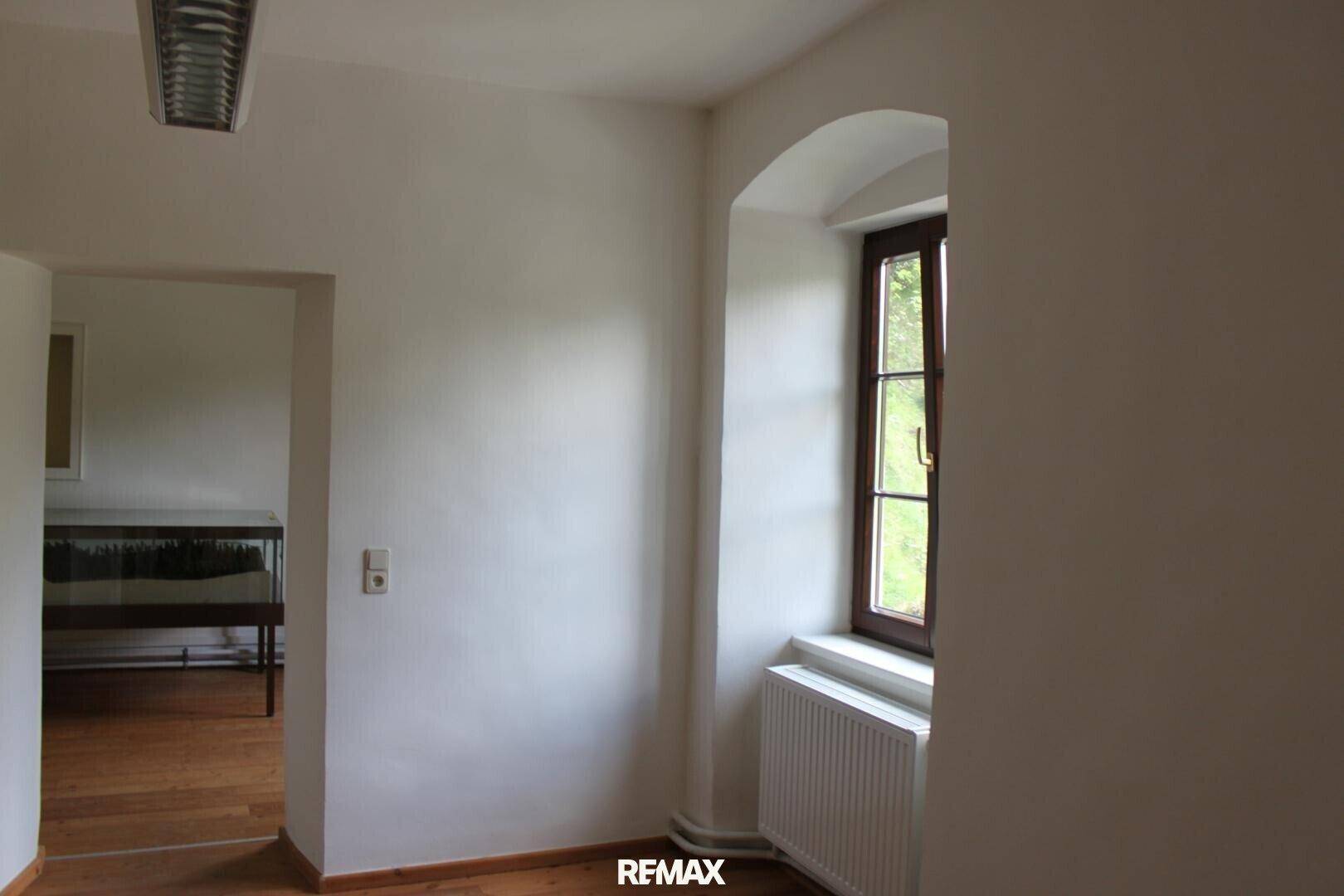 Heller Raum mit Holzboden, weiß gestrichenen Wänden und einem Fenster mit tiefer Laibung.