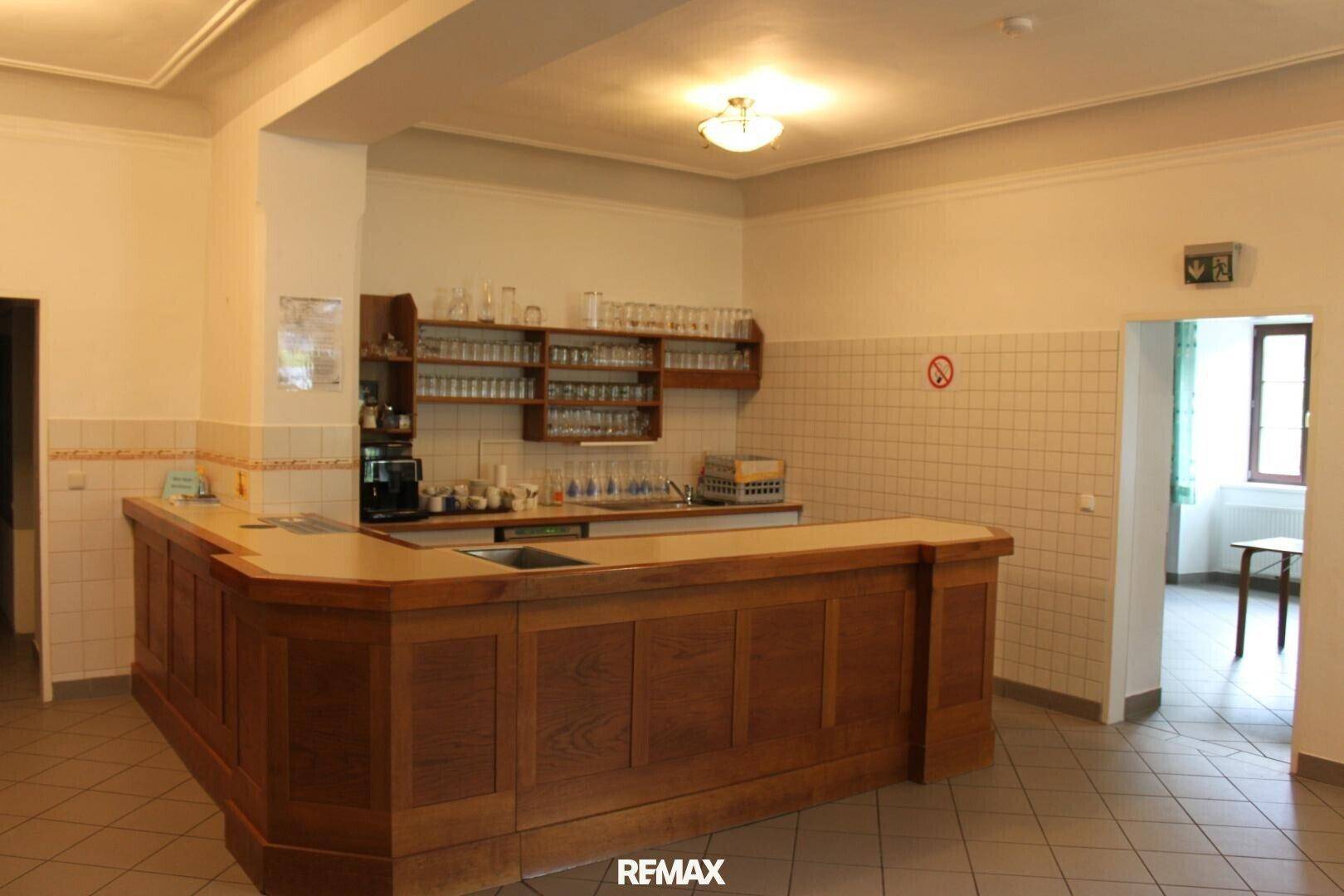 Bar-Bereich mit Holztheke, Fliesenboden und Regalen voller Gläser, bereit für Gäste.