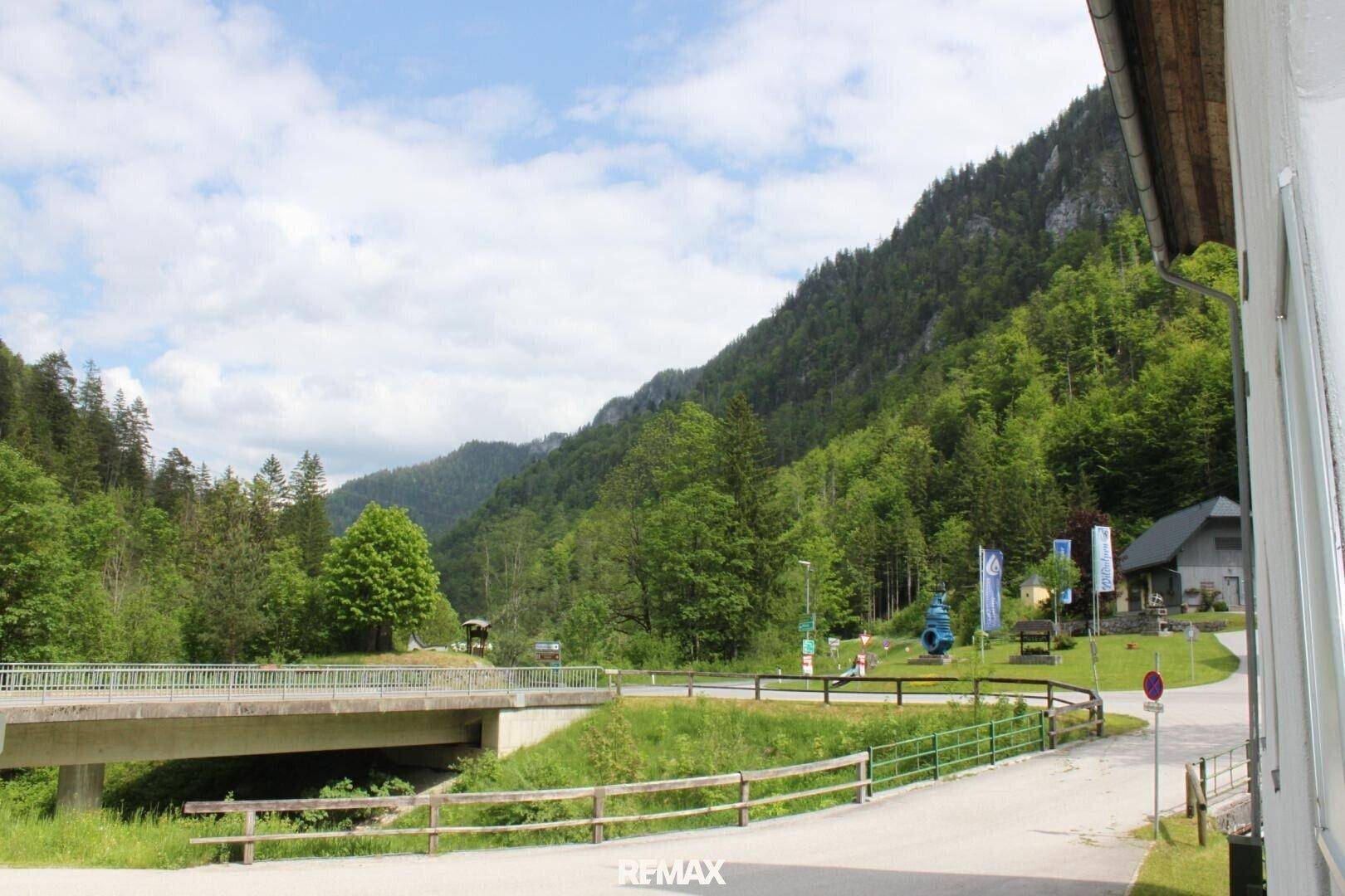 Malerische Berglandschaft mit üppigem Grün, einem Fluss und einer Brücke unter blauem Himmel.