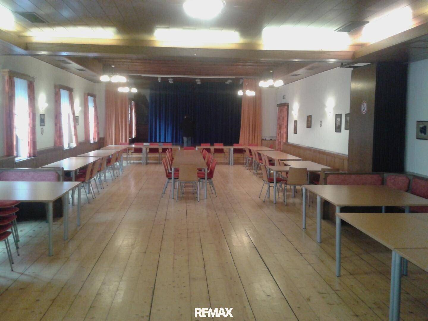 Geräumiger Speisesaal mit Holzboden und Holzbalkendecke, ausgestattet mit Tischen und Bänken.