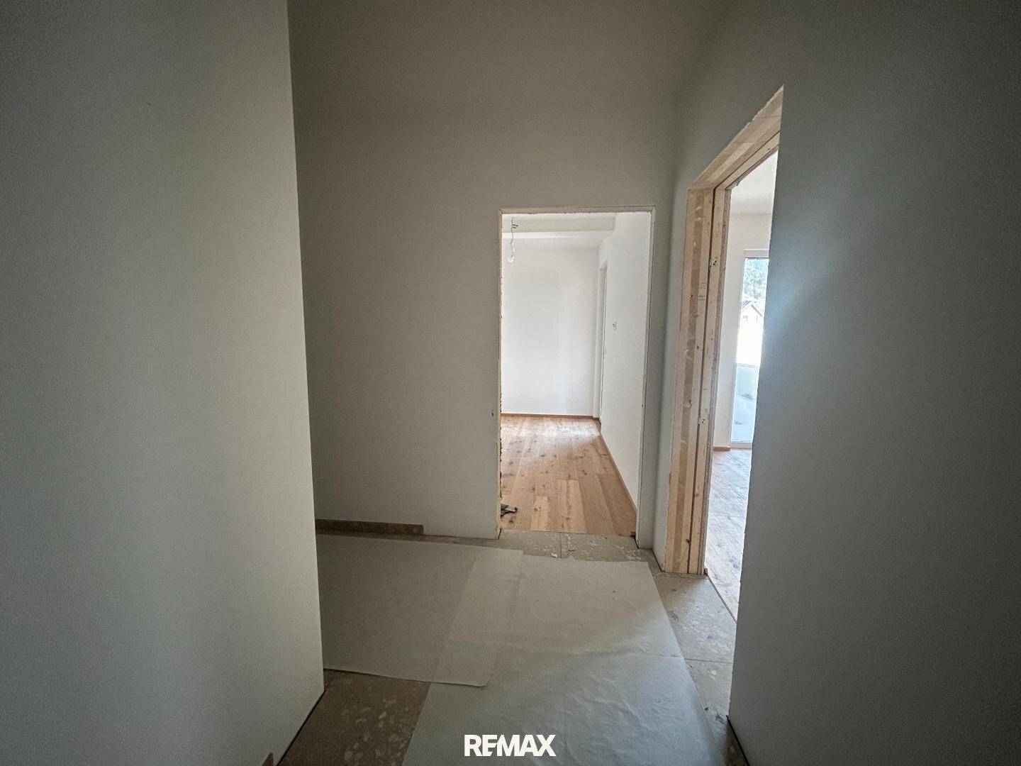 Flur in der Bauphase mit weißen Wänden und Blick in angrenzende Zimmer.