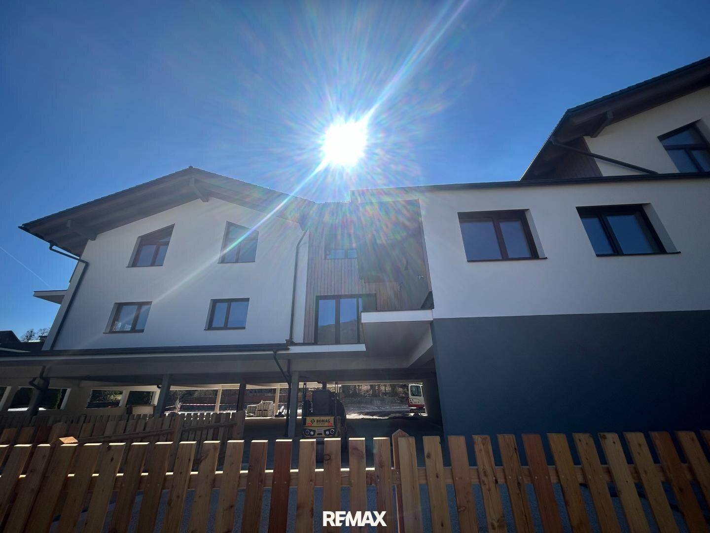 Neubau mit weißer Fassade, Holzdetails und Balkonen unter strahlend blauem Himmel.