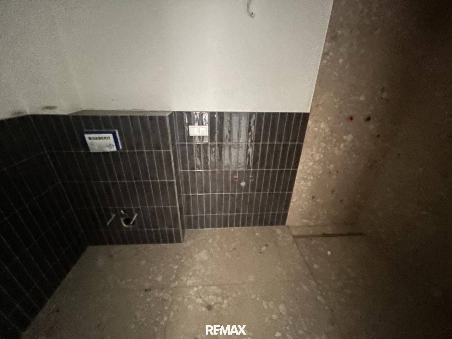 Unfertiges Badezimmer mit dunklen Wandfliesen und vorbereiteten Installationen.