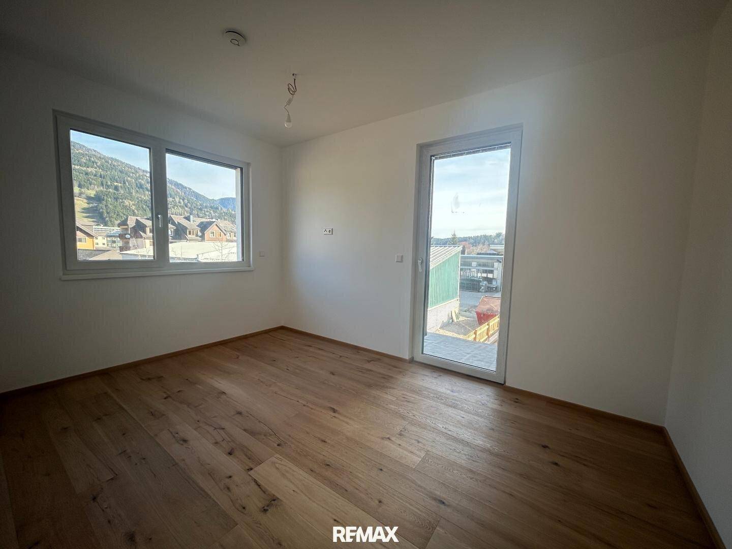 Helles Zimmer mit Parkettboden und zwei Fenstern, die viel Tageslicht hereinlassen.