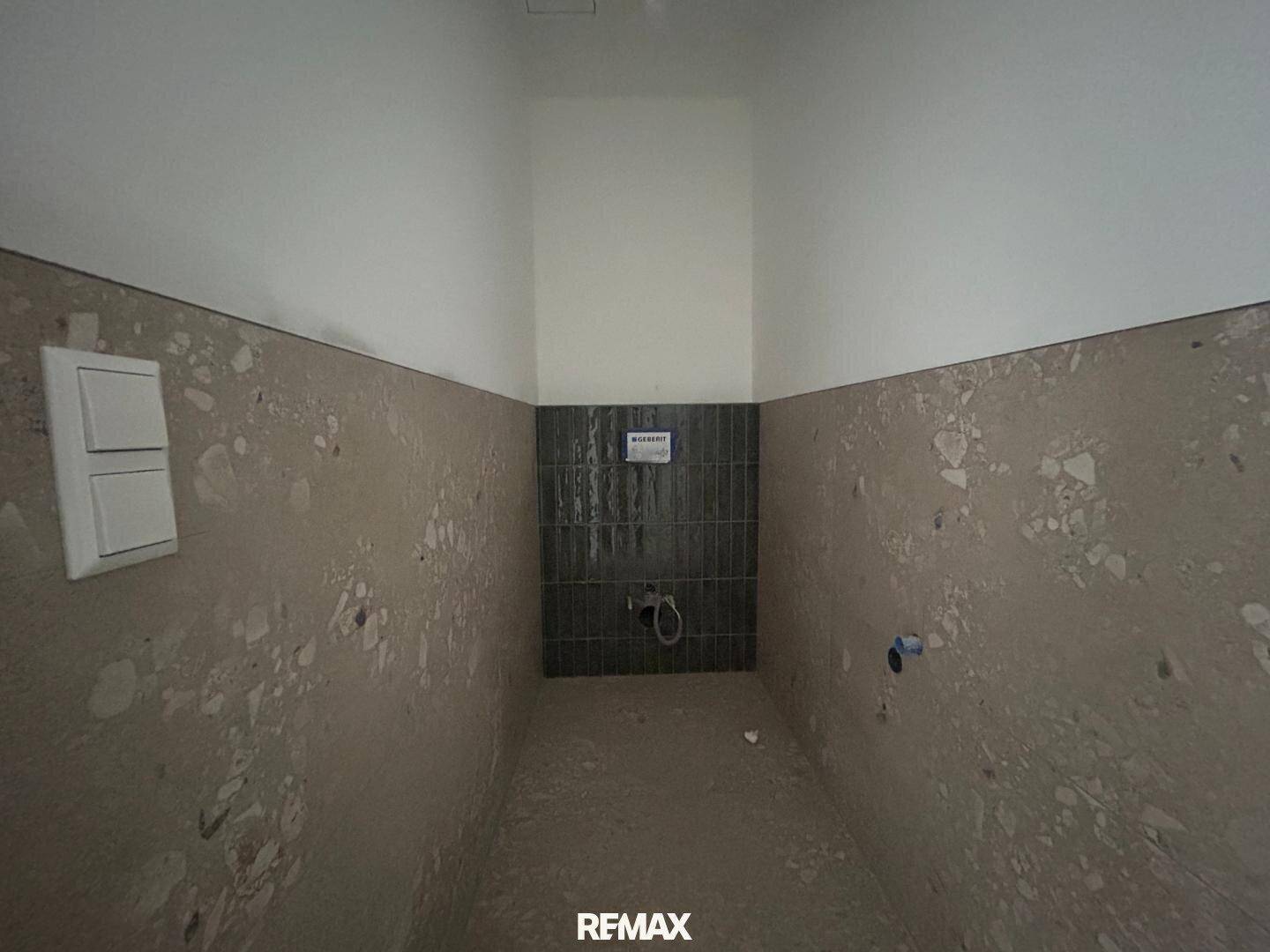 Unfertiges Badezimmer mit gefliesten Wänden und vorbereiteten Anschlüssen für Sanitäranlagen.