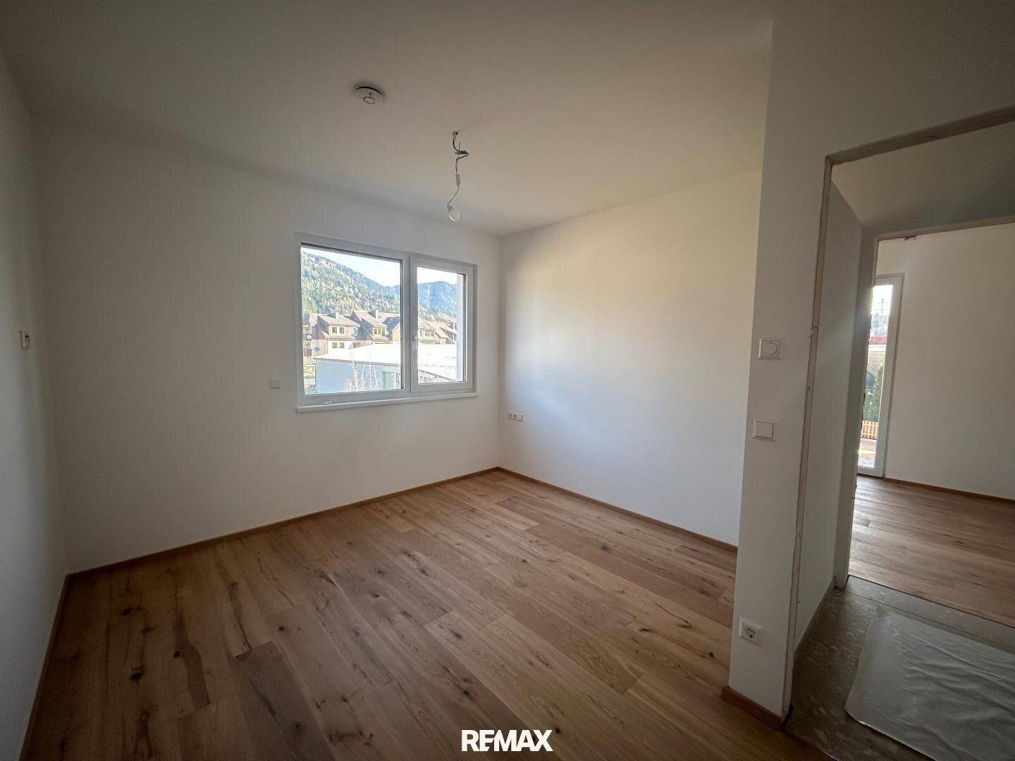 Geräumiges Zimmer mit Holzboden und einem großen Fenster, ideal als Schlafzimmer.
