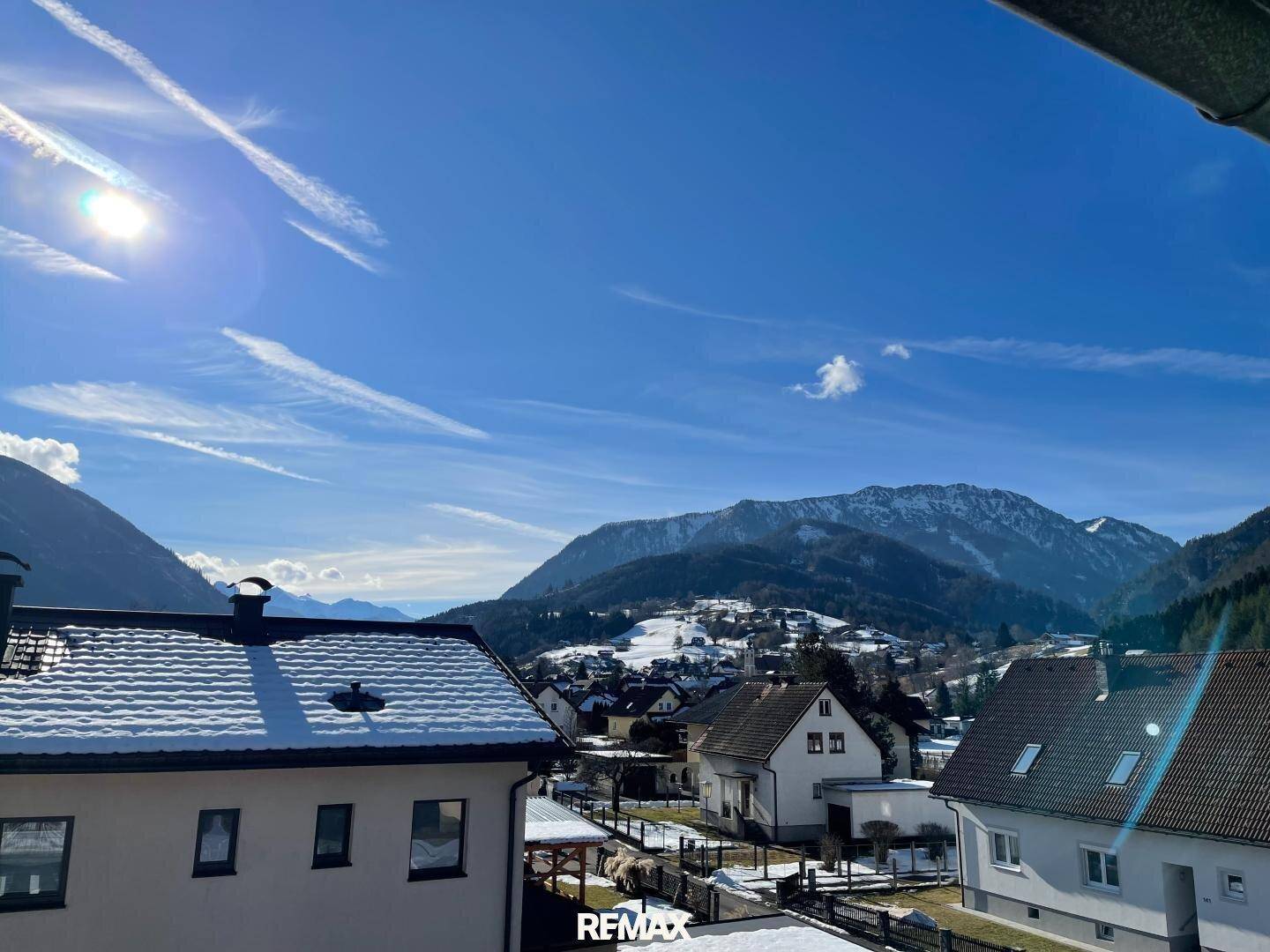 Panoramablick auf ein verschneites Dorf und die umliegende Berglandschaft unter blauem Himmel.