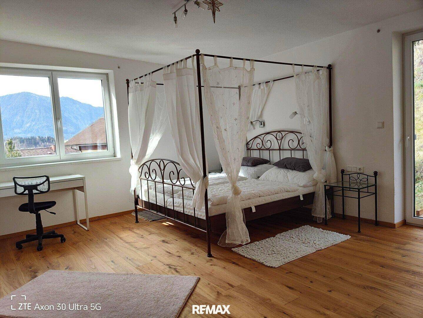 Helles Schlafzimmer mit Himmelbett, Holzboden, Schreibtisch und großem Fenster mit Bergblick.