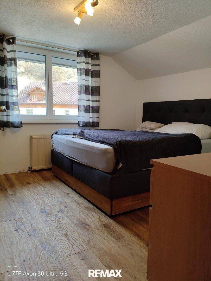 Schlafzimmer mit Bett, Holzboden und Fenster mit gestreiften Vorhängen unter einer Dachschräge.