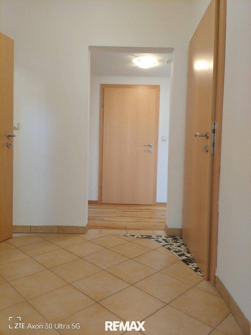 Flur mit Fliesenboden, der in einen Bereich mit Holzboden übergeht, und Holztüren.