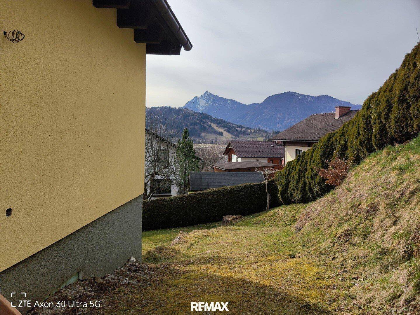 Gartenbereich am Hang mit Hecke und beeindruckendem Blick auf die Berglandschaft.