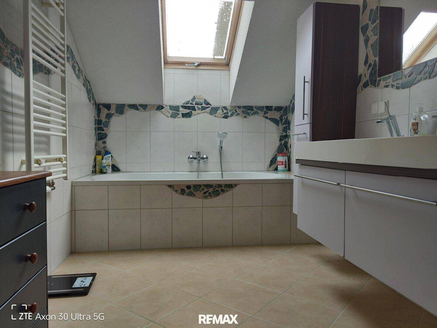 Geräumiges Badezimmer mit Badewanne, Waschtisch, Handtuchheizkörper und Dachfenster unter einer Dachschräge.