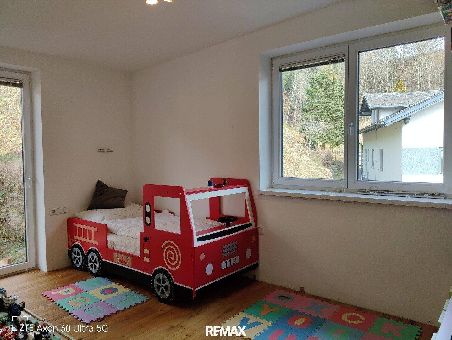 Kinderzimmer mit einem Feuerwehrauto-Bett, Holzboden und einem großen Fenster.
