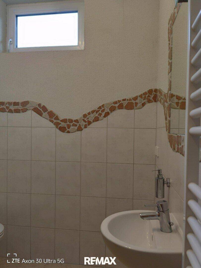 Badezimmer mit Waschbecken, Spiegel, Handtuchheizkörper und einem kleinen Fenster.