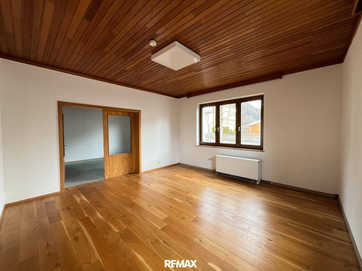 Heller Raum mit Holzboden, Holzdecke und einem Fenster, das Tageslicht hereinlässt.