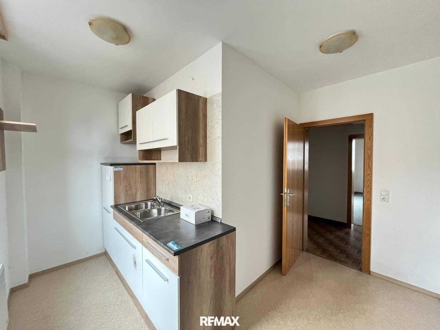 Kleine Küchenzeile mit modernen Schränken in Weiß und Holzoptik, Spüle und Kühlschrank.
