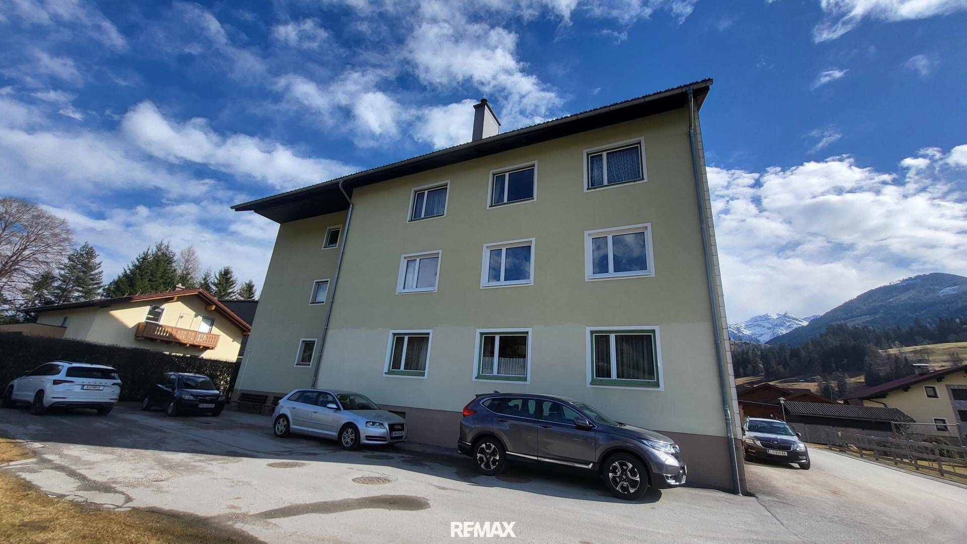 Wohngebäude mit Parkplätzen davor und Blick auf die umliegende Berglandschaft.