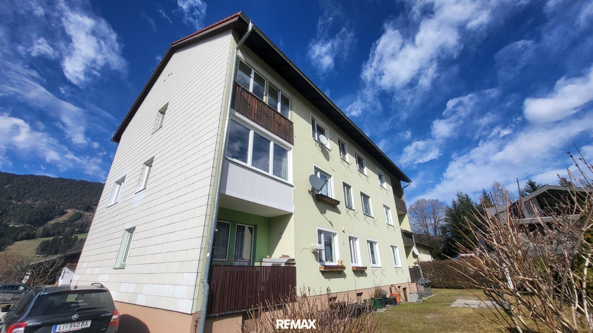 Seitenansicht des Wohngebäudes mit schrägem Dach und Balkonen unter blauem Himmel.