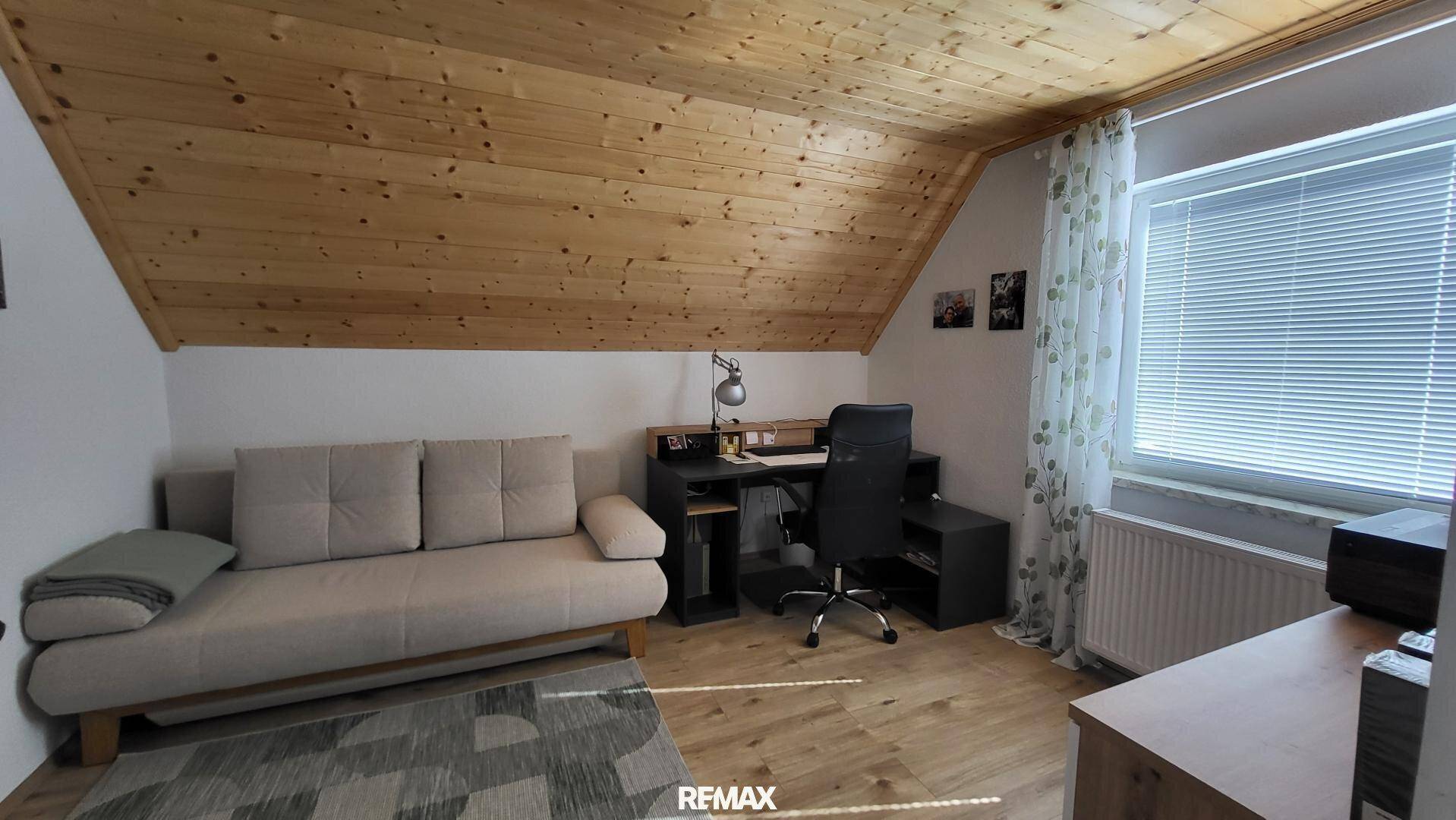 Dachgeschosszimmer mit Holzdecke, Schlafsofa, Schreibtisch und Fenster für natürliches Licht.
