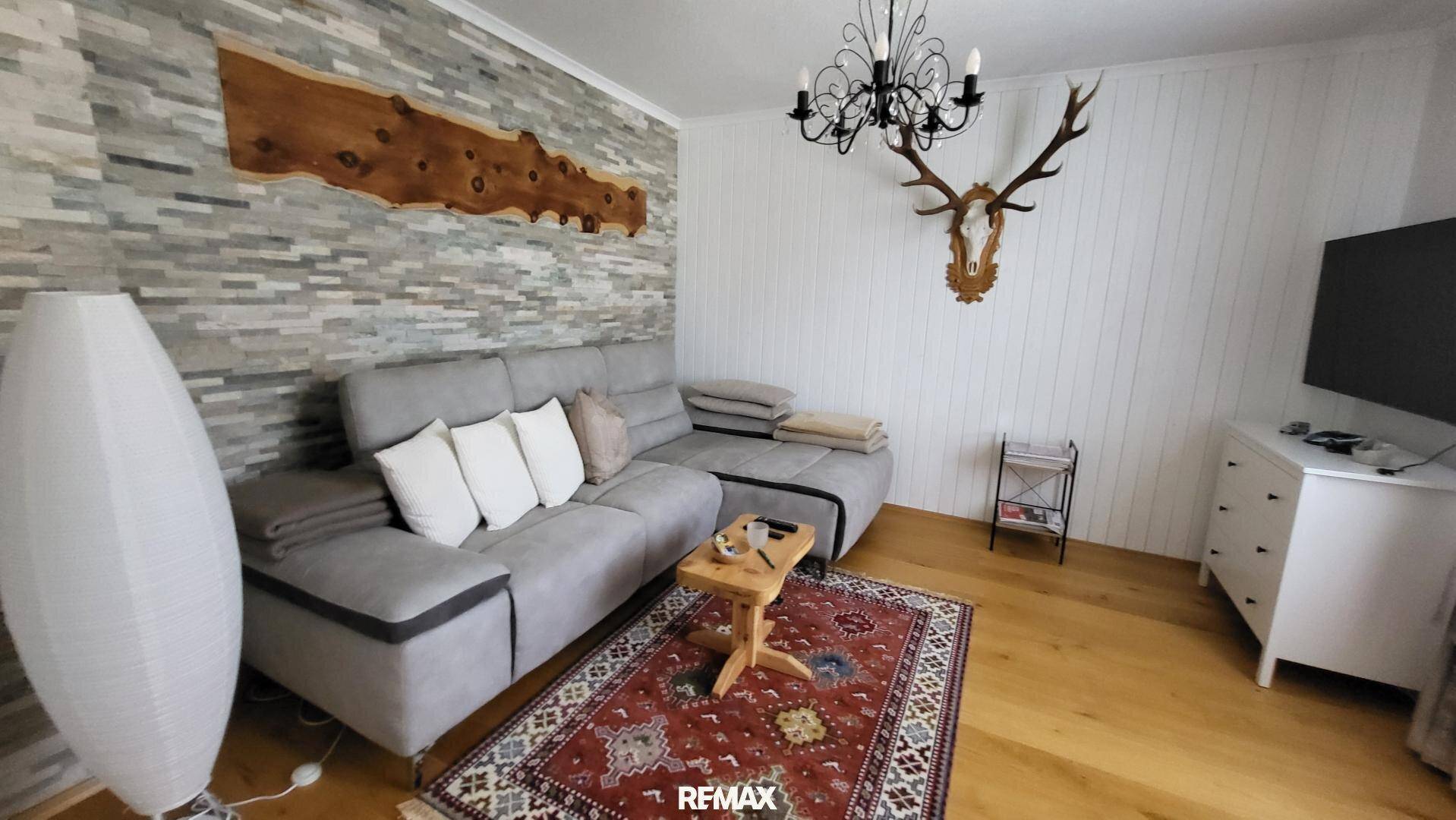 Gemütliches Wohnzimmer mit Steinfassade, Ecksofa, Holzboden und traditioneller Hirschgeweih-Dekoration.