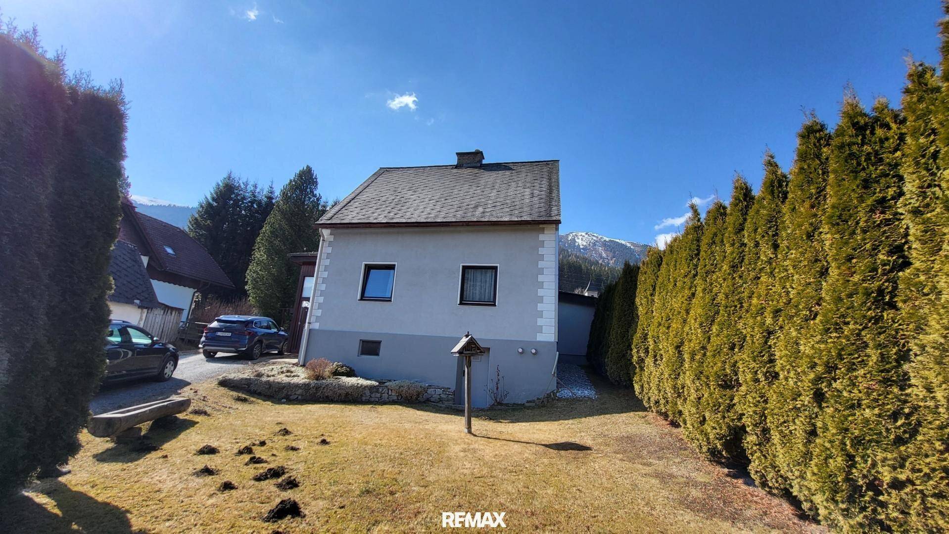 Rückansicht des Hauses mit gepflegtem Gartenbereich, hoher Hecke und Blick auf die umliegenden Berge.