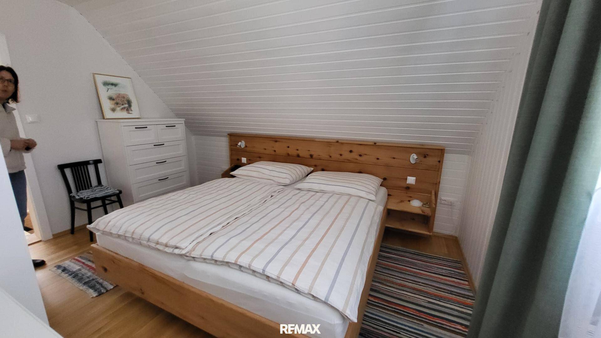 Helles Schlafzimmer im Dachgeschoss mit Holzbett, weiß getäfelter Schräge und Holzboden.