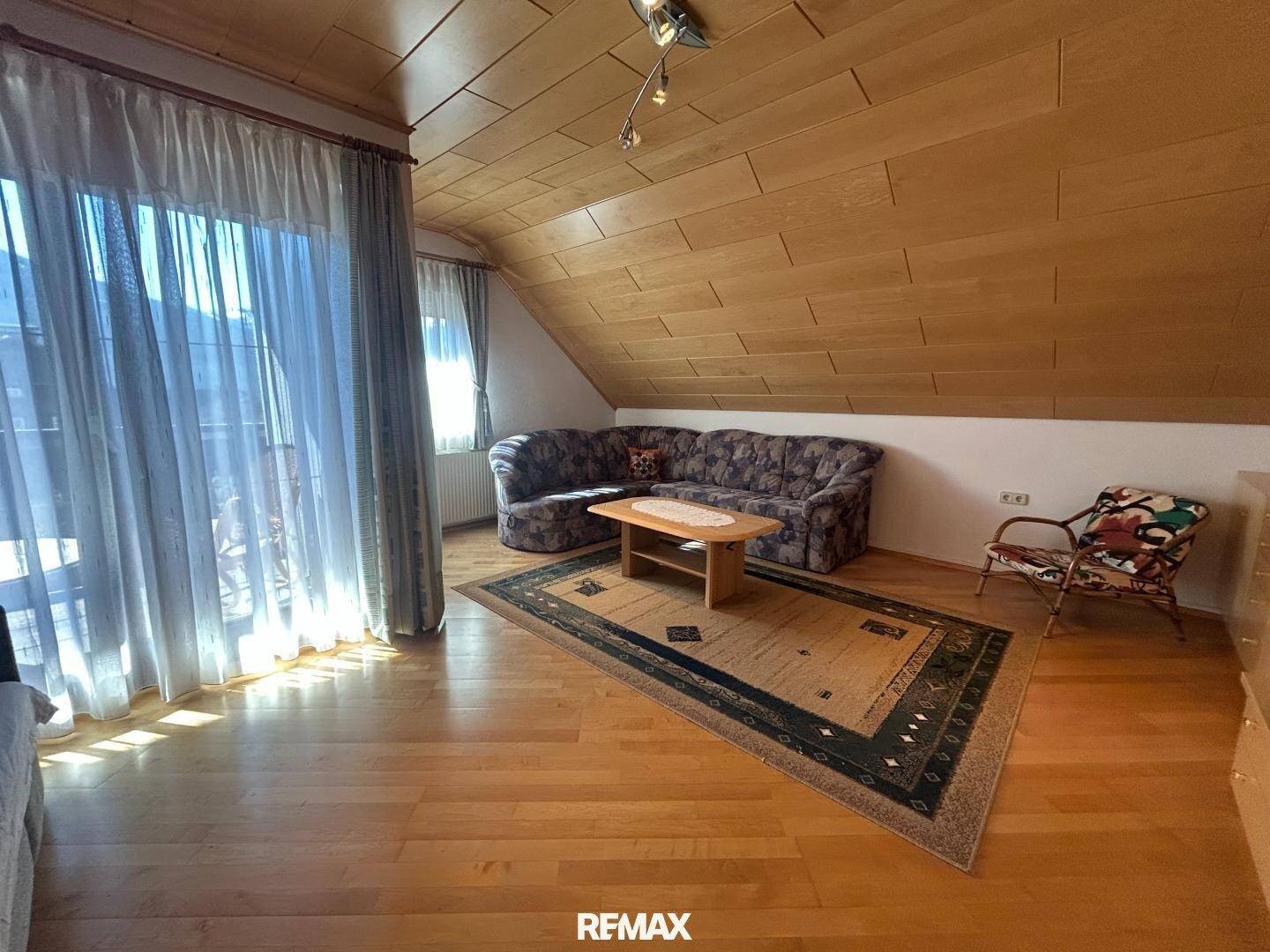 Geräumiges Wohnzimmer im Dachgeschoss mit Sofa, Teppich und Zugang zu einem Balkon.
