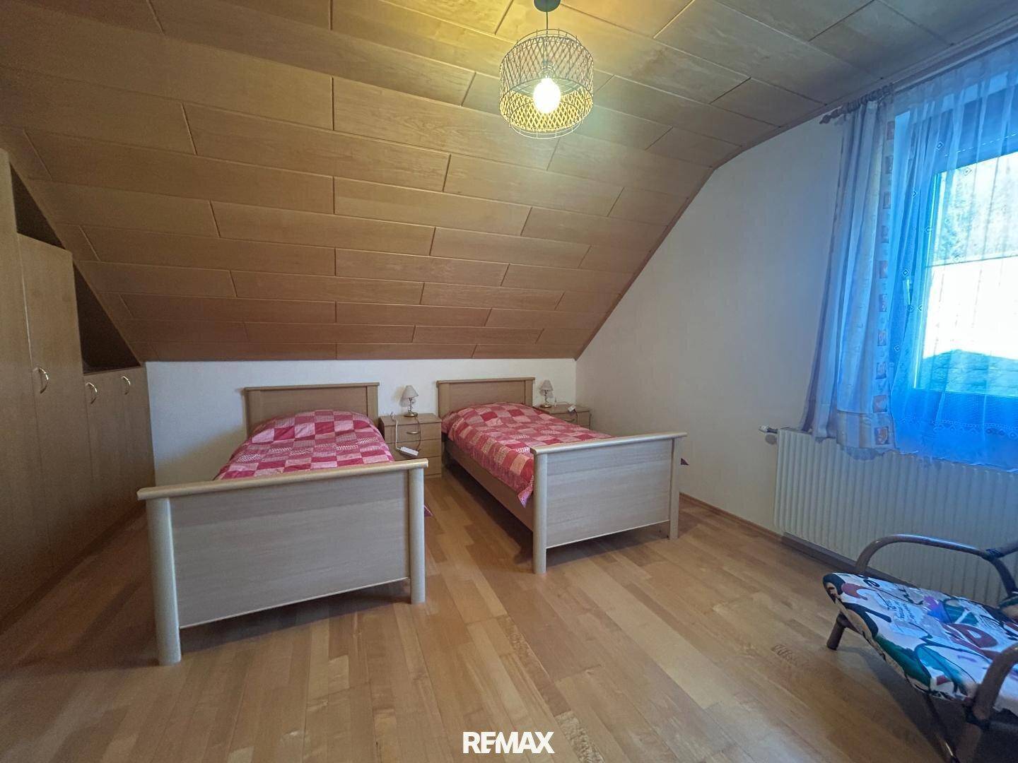 Helles Schlafzimmer im Dachgeschoss mit zwei Einzelbetten, Holzdecke und schrägen Wänden.