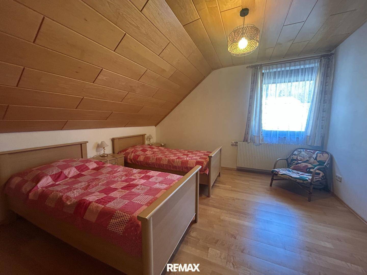 Dachgeschoss-Schlafzimmer mit zwei Einzelbetten, Holzverkleidung und einem Fenster für Tageslicht.