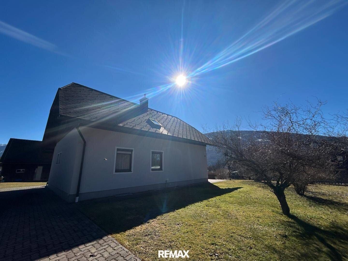 Seitenansicht des Hauses mit gepflastertem Weg und einem sonnigen Gartenbereich.