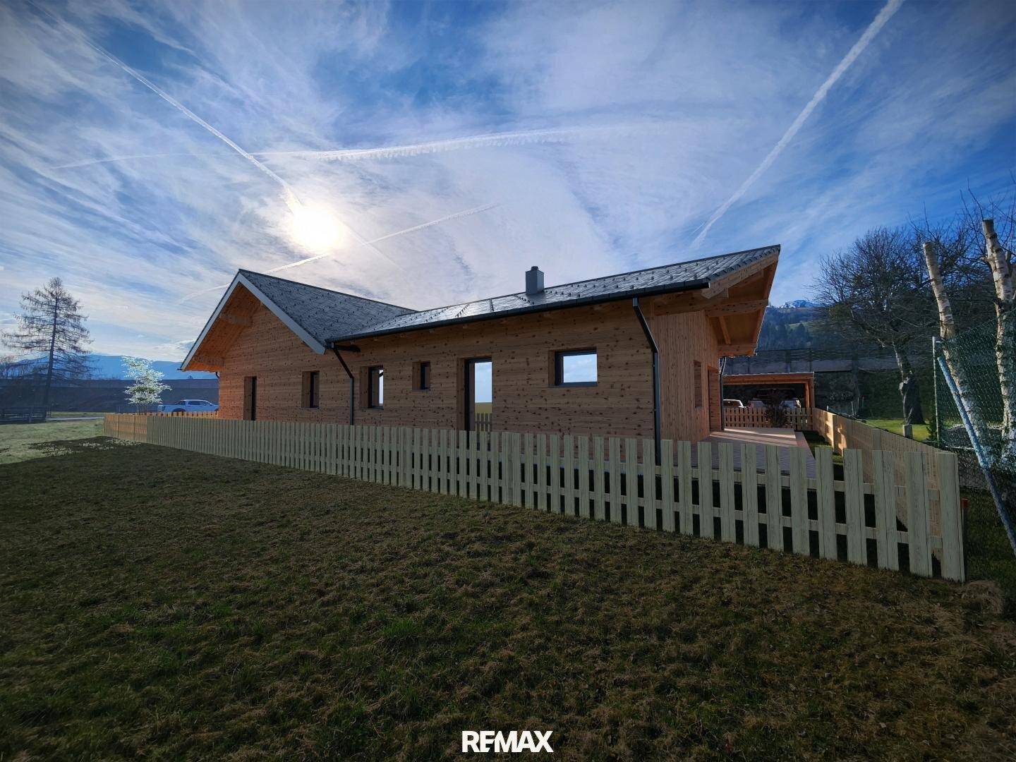 Modernes Holzhaus mit Satteldach und Photovoltaikanlage, umgeben von einem grünen Garten.