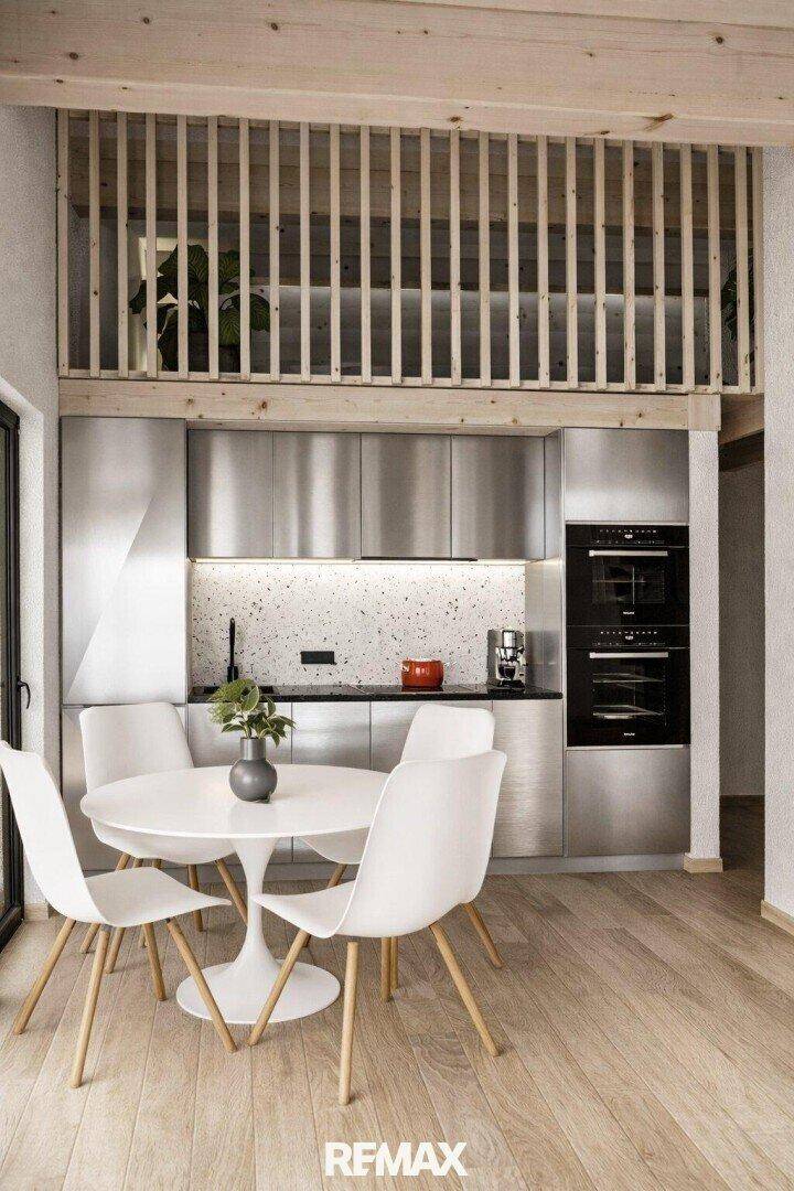 Heller Essbereich mit modernem Tisch und Stühlen neben einer Küche unter einem Holz-Loft.