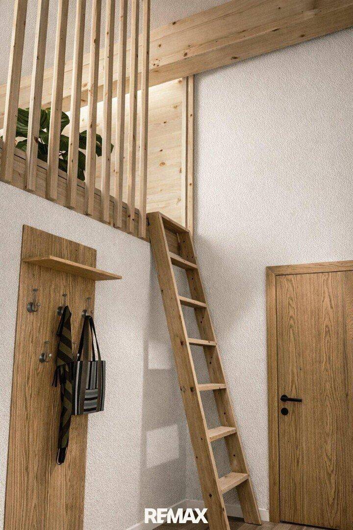 Holzleiter führt zu einem oberen Loftbereich mit Garderobe im Eingangsbereich.