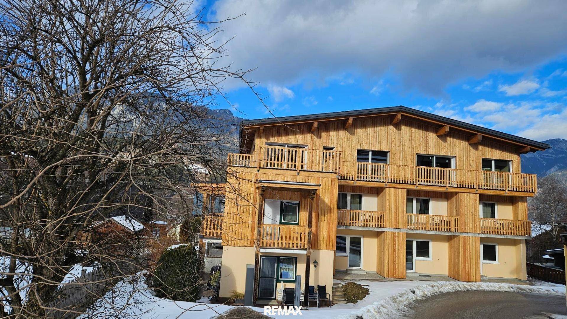 Modernes Gebäude mit Holzfassade und Balkonen in alpiner Umgebung, umgeben von Schnee.