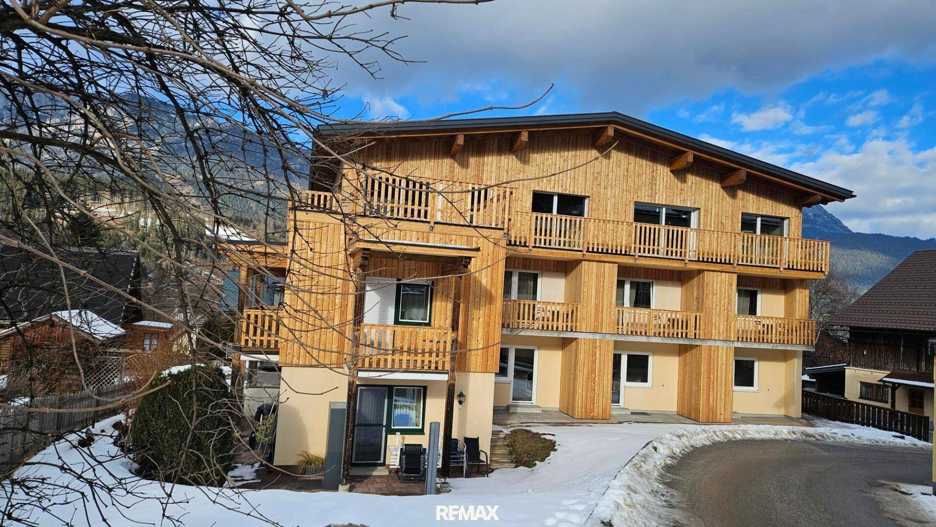Attraktives Mehrfamilienhaus mit Holzfassade und Balkonen, eingebettet in eine winterliche Berglandschaft.