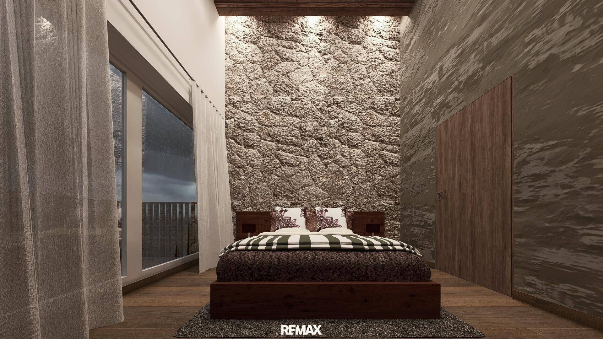 Schlafzimmer mit Steinwand, Holzboden und großen Fenstern, die viel Licht hereinlassen.