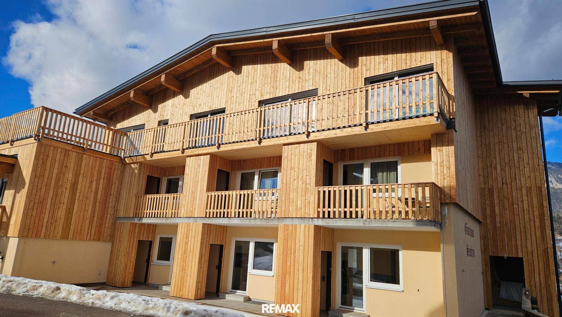 Neubau mit moderner Holzverkleidung und mehreren Balkonen, umgeben von Schnee und Bergen.