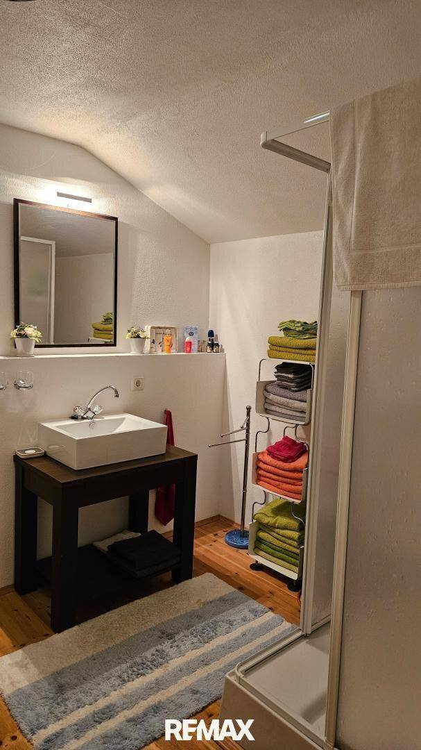 Helles Badezimmer im Dachgeschoss mit Waschbecken, Dusche und Holzfußboden.