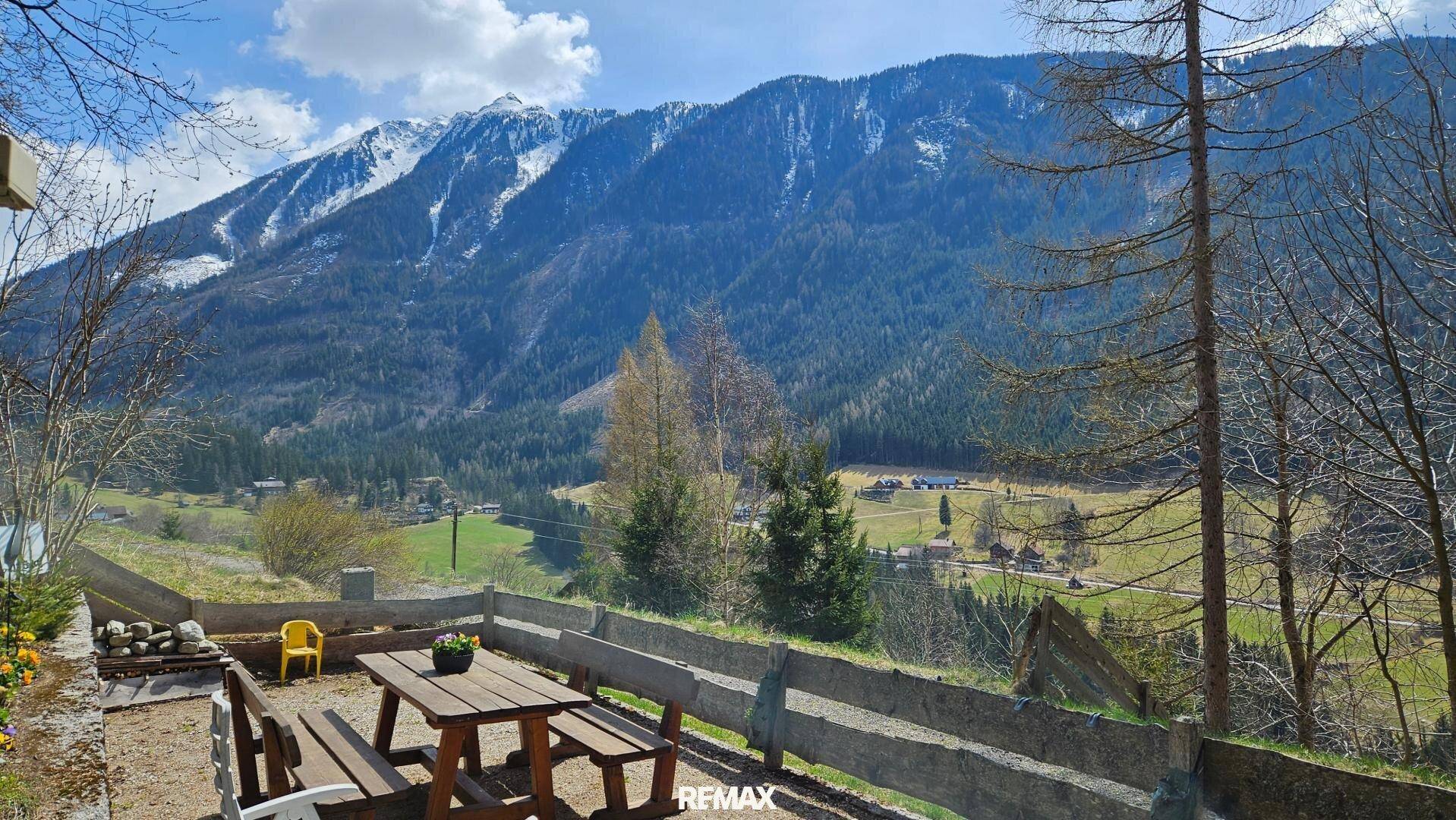 Gemütlicher Außenbereich mit Holztisch und Bänken, bietet einen weiten Blick auf die umliegenden Berge und das Tal.