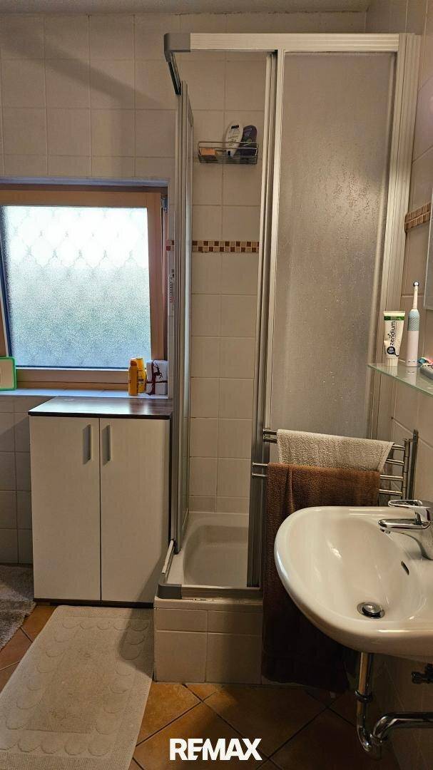 Funktionales Badezimmer mit Dusche, Waschbecken und Fenster, in gutem Zustand.