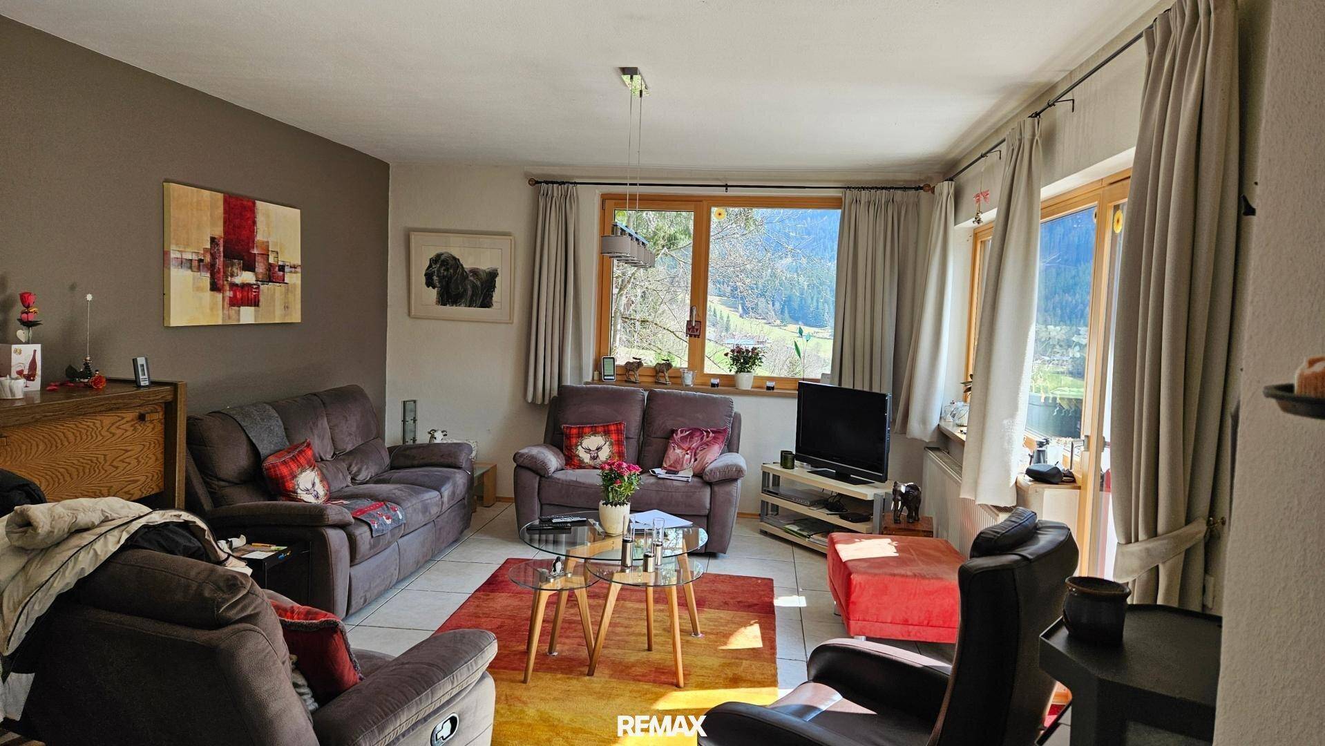 Geräumiges Wohnzimmer mit bequemen Sofas, Fliesenboden und Blick ins Grüne.