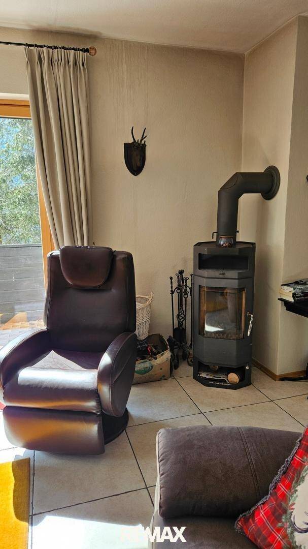 Gemütliches Wohnzimmer mit Kaminofen, Sessel und Blick ins Grüne durch die Fenster.