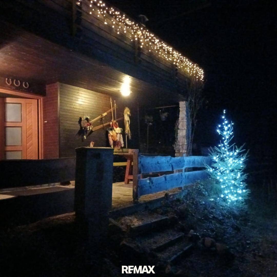 Eingangsbereich des Hauses bei Nacht, beleuchtet mit Lichterketten und einem geschmückten Weihnachtsbaum.