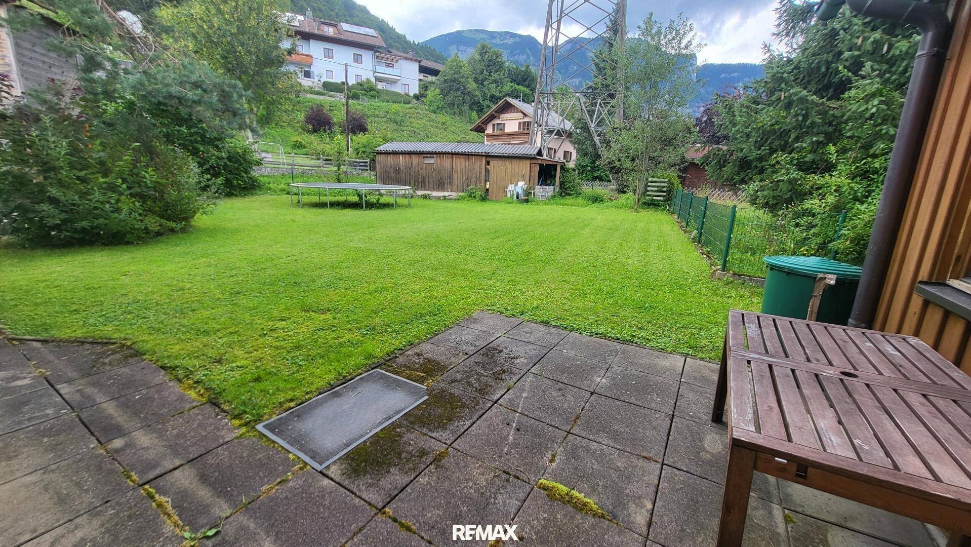 Großer Garten mit Rasenfläche, gepflastertem Sitzbereich und Blick auf die umliegenden Berge.