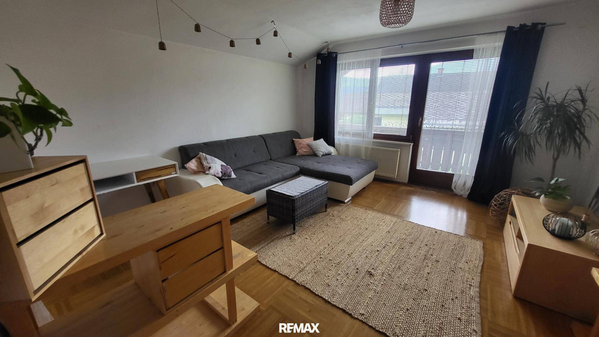 Helles Wohnzimmer mit modernem Ecksofa, Holzboden und Zugang zu einem Außenbereich.