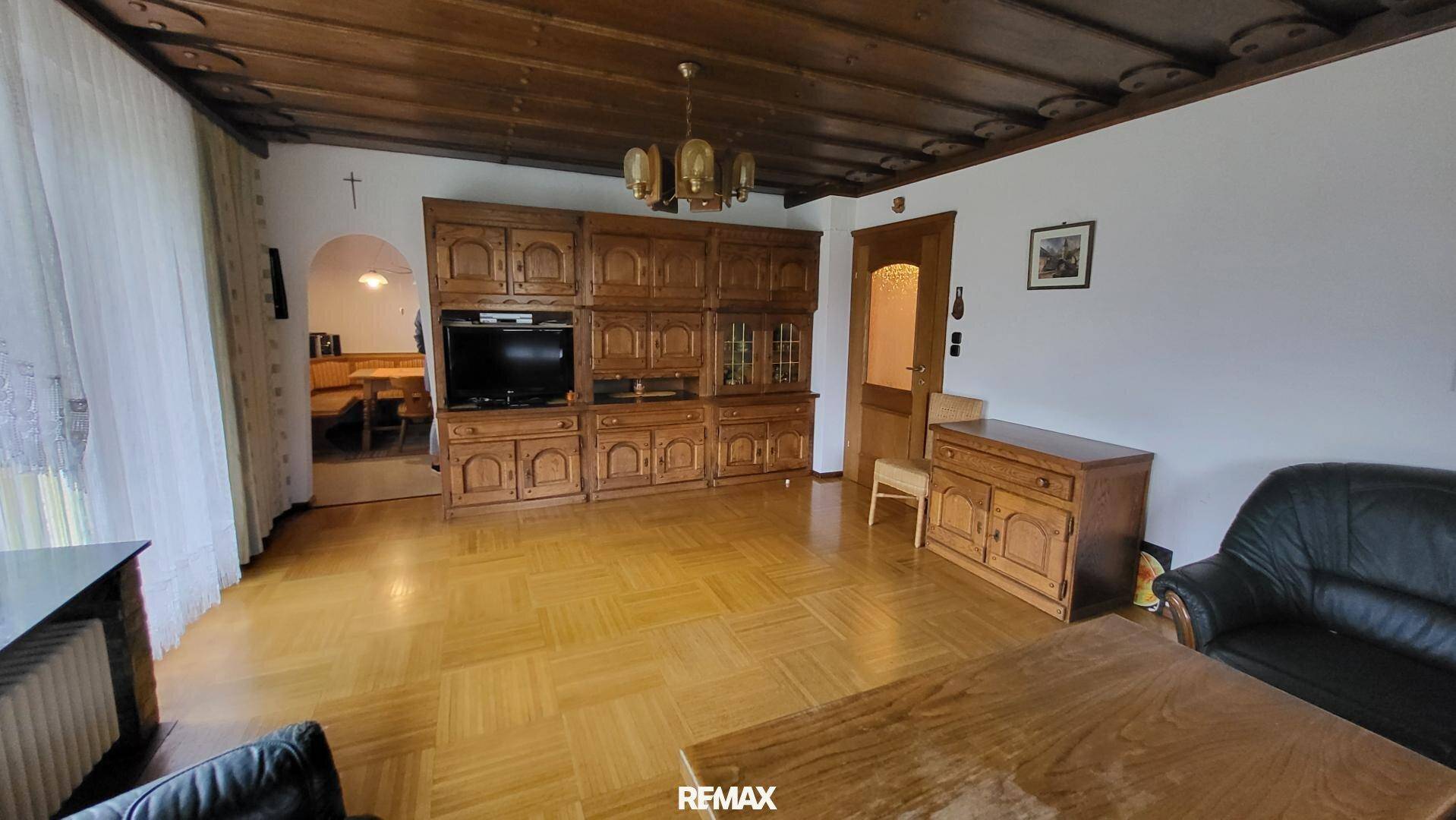 Geräumiges Wohnzimmer mit traditionellen Holzmöbeln, Parkettboden und einer charakteristischen Holzdecke.
