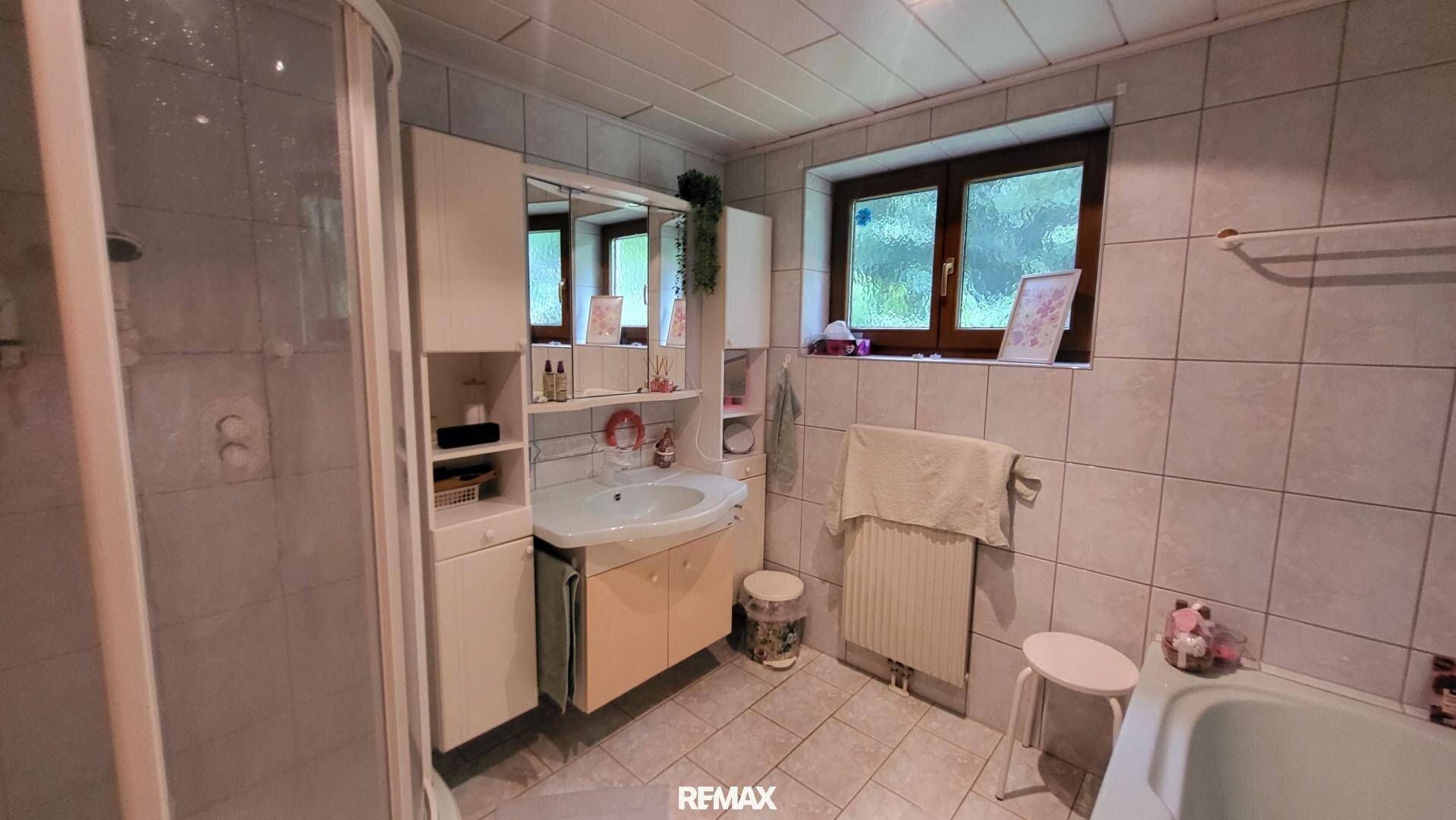 Helles Badezimmer mit Dusche, Badewanne, Einzelwaschbecken und Fenster für Tageslicht.